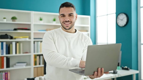 Jonge Spaanse man student glimlacht vol vertrouwen met behulp van laptop op de bibliotheek universiteit - Foto, afbeelding