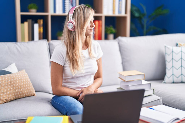 Jonge blonde vrouw studeren met behulp van computer laptop thuis op zoek naar kant, ontspannen profiel poseren met natuurlijke gezicht en zelfverzekerde glimlach.  - Foto, afbeelding