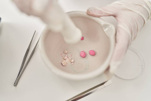 Молода красива іспаномовна жінка вчений подрібнює таблетки на мисці в лабораторії
 - Фото, зображення