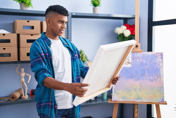 młody Latynos człowiek artysta uśmiechnięty pewny siebie patrząc rysować w studio sztuki - Zdjęcie, obraz