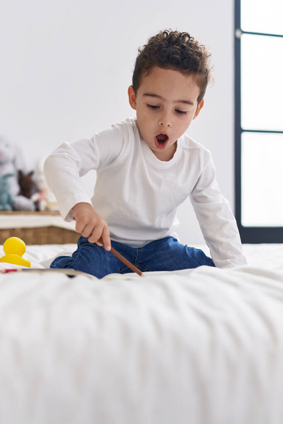 Adorable hispanic boy preschool student sitting on bed drawing on notebook at bedroom - Photo, Image
