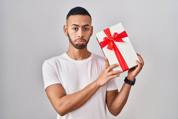 Young hispanic man holding presents depressed and worry for distress, crying angry and afraid. sad expression.  - Φωτογραφία, εικόνα