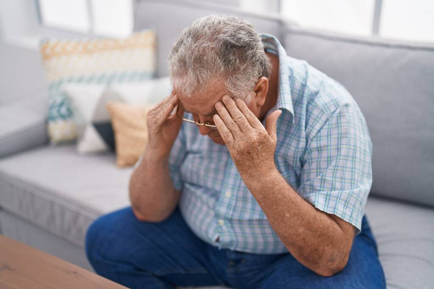 Keski-ikäinen harmaa tukka mies stressaantunut istuu sohvalla kotona - Valokuva, kuva