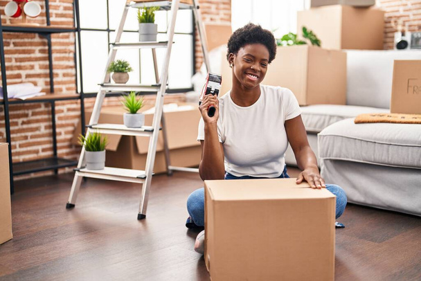 mujer afroamericana embalaje caja de cartón sentado en el piso en el nuevo hogar - Foto, Imagen