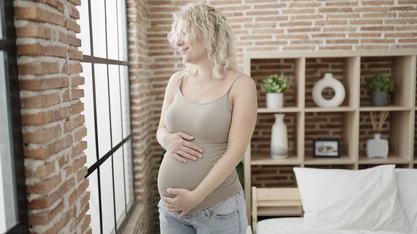 Young pregnant woman touching belly standing at bedroom - Zdjęcie, obraz