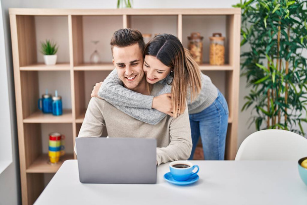 Άνδρας και γυναίκα ζευγάρι αγκαλιάζονται χρησιμοποιώντας φορητό υπολογιστή στο σπίτι - Φωτογραφία, εικόνα