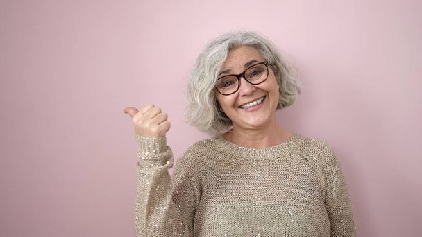 Mulher de meia-idade com cabelos grisalhos sorrindo confiante apontando para o lado sobre fundo rosa isolado - Foto, Imagem