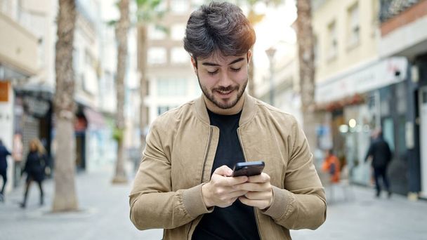 Νεαρός Ισπανός που χρησιμοποιεί smartphone χαμογελώντας στο δρόμο - Φωτογραφία, εικόνα