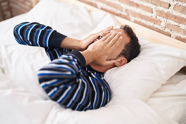Young hispanic man stressed lying on bed at bedroom - Photo, Image