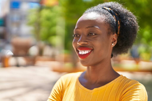 Αφροαμερικανή γυναίκα χαμογελά σίγουρος κοιτάζοντας προς την πλευρά στο πάρκο - Φωτογραφία, εικόνα