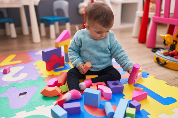 Adorable hispanic baby playing with construction blocks sitting on floor at kindergarten - 写真・画像