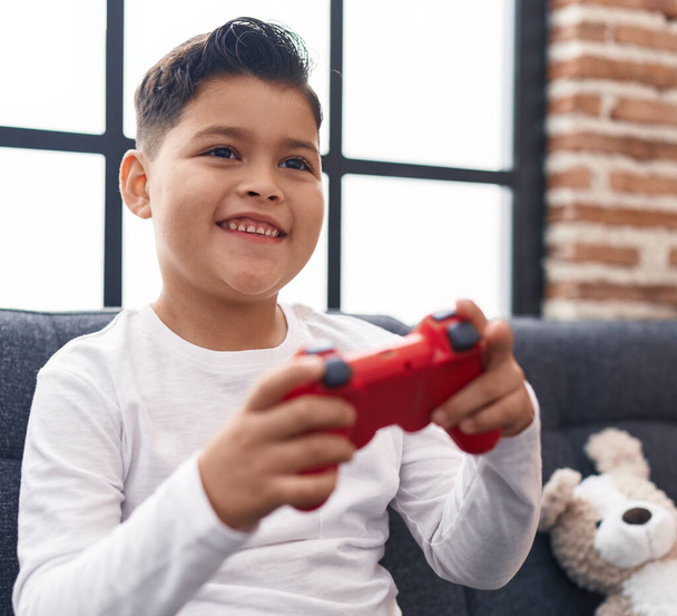 Чарівний іспаномовний хлопчик грає в відеоігри, сидячи на дивані вдома
 - Фото, зображення