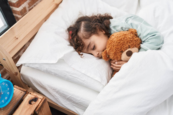 Adorable hispanic girl hugging teddy bear lying on bed sleeping at bedroom - Photo, Image