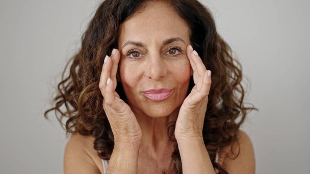 Moyen Age femme hispanique souriant confiant appliquer un traitement de la peau sur fond blanc isolé - Photo, image
