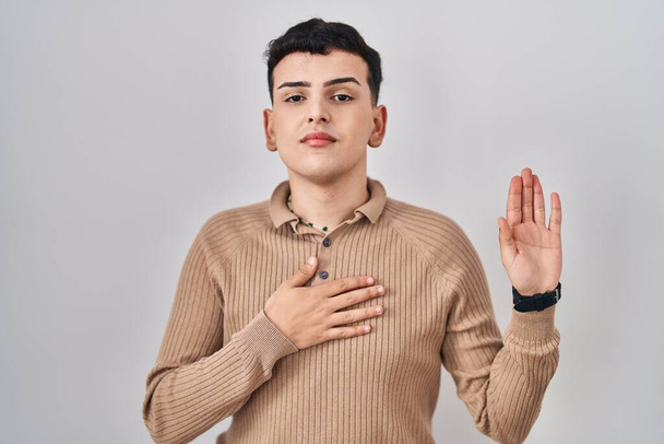 Non binary person standing over isolated background swearing with hand on chest and open palm, making a loyalty promise oath  - Photo, Image
