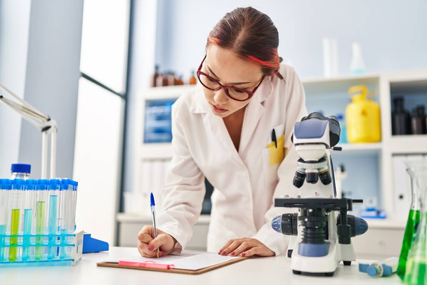 Young caucasian woman scientist writing report working at laboratory - Foto, Bild