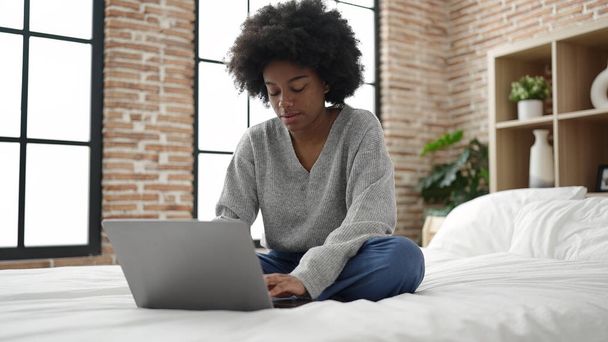Femme afro-américaine utilisant un ordinateur portable assis sur le lit dans la chambre - Photo, image