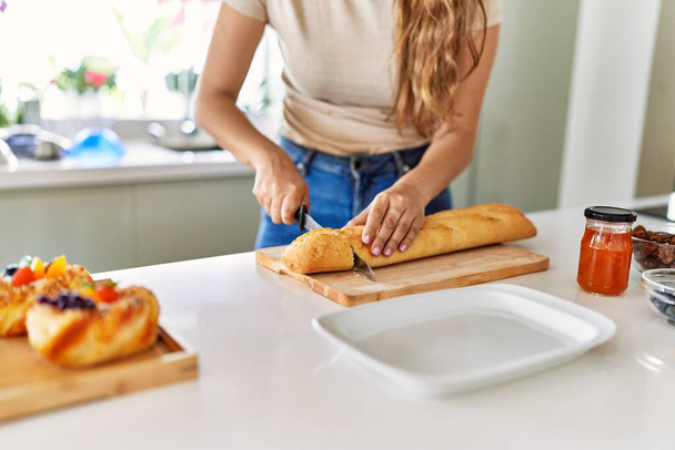Junge schöne hispanische Frau bereitet Frühstück beim Brotschneiden in der Küche zu - Foto, Bild