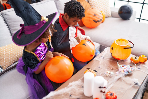 Adorable african american boy and girl having halloween party drawing on balloon at home - Фото, изображение