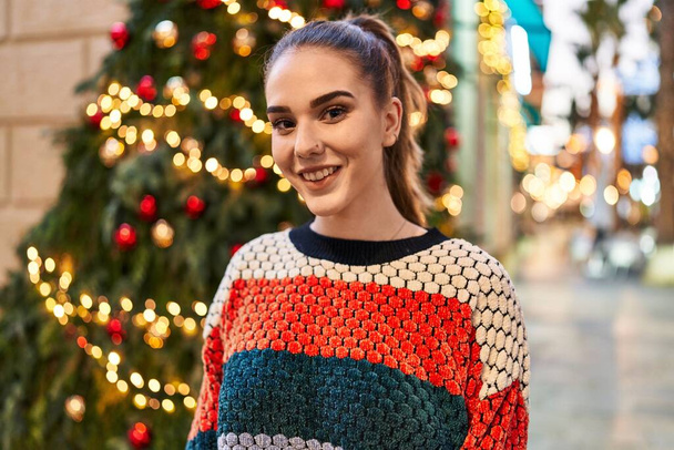 Young woman smiling confident standing by christmas tree at street - Fotoğraf, Görsel
