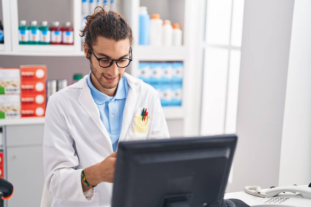 Young hispanic man pharmacist using smartphone working at pharmacy - Fotó, kép