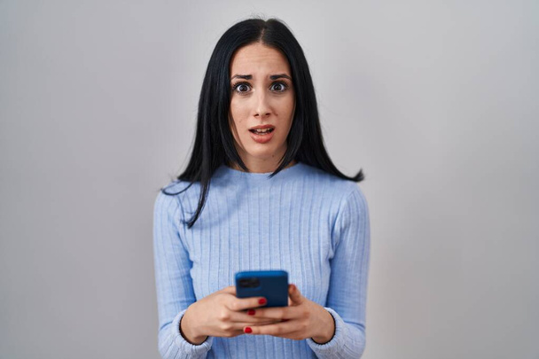Hispanic woman using smartphone clueless and confused expression. doubt concept.  - Foto, immagini