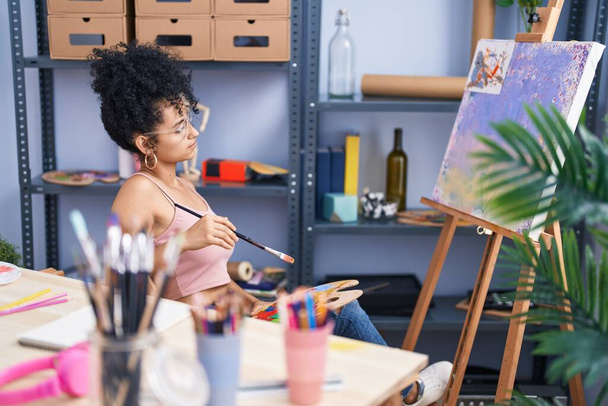 若いヒスパニック系の女性アーティストがアートスタジオで疑わしい表現で描く - 写真・画像