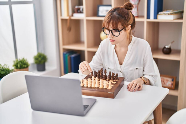 Νεαρή γυναίκα παίζει online παιχνίδι σκάκι στο σπίτι - Φωτογραφία, εικόνα