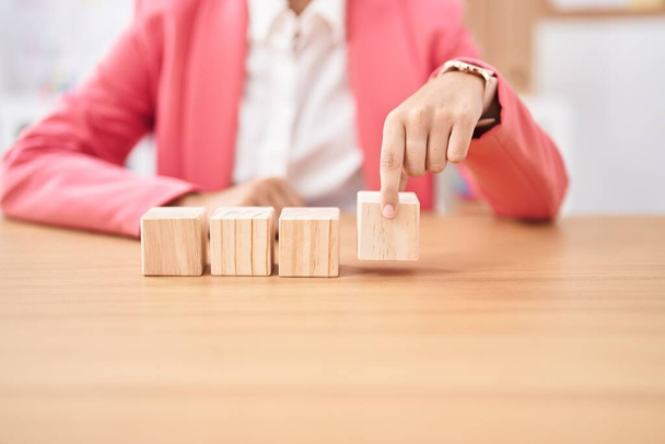 Young beautiful hispanic woman business worker sitting on table with wooden cubes at office - Foto, immagini
