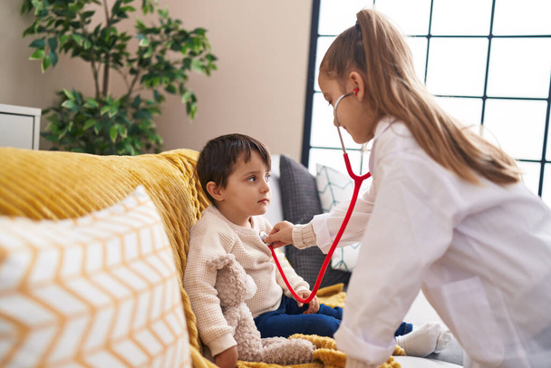 Uroczy chłopiec i dziewczyna w mundurze lekarza badający stetoskop w domu - Zdjęcie, obraz