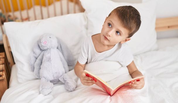 Adorabile caucasico ragazzo lettura libro seduto sul letto in camera da letto - Foto, immagini