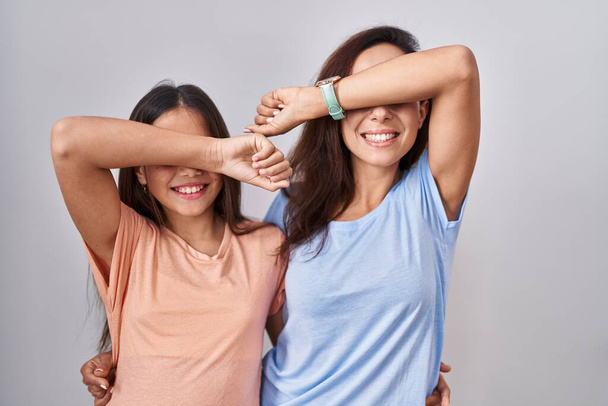 Young mother and daughter standing over white background smiling cheerful playing peek a boo with hands showing face. surprised and exited  - Photo, Image