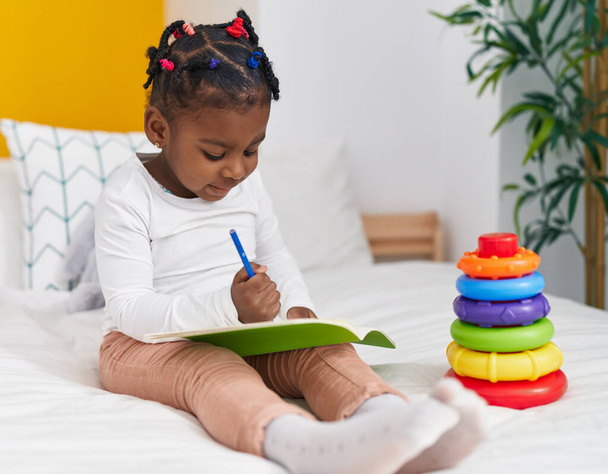 African american girl sitting on bed drawing on notebook at bedroom - Photo, Image