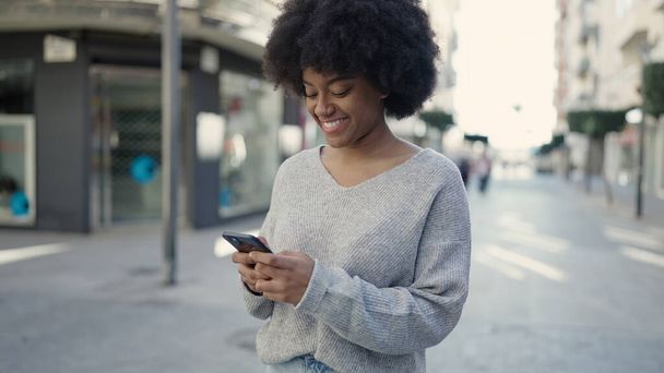 アフリカ系アメリカ人の女性が路上でスマートフォンを使って笑顔で - 写真・画像