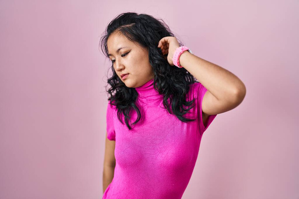 Joven mujer asiática de pie sobre fondo rosa que se extiende hacia atrás, cansado y relajado, soñoliento y bostezando por la mañana temprano  - Foto, imagen