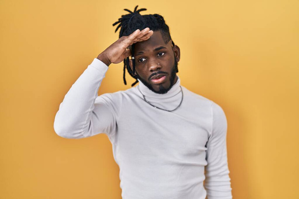 African man with dreadlocks wearing turtleneck sweater over yellow background worried and stressed about a problem with hand on forehead, nervous and anxious for crisis  - Foto, Bild