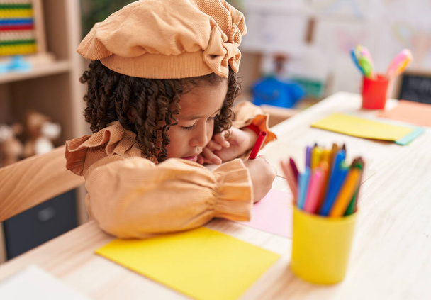 アフリカ系アメリカ人の少女就学前の生徒が幼稚園で紙の上に座っている - 写真・画像