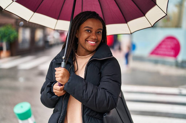 African american woman smiling confident using umbrella at street - Fotoğraf, Görsel