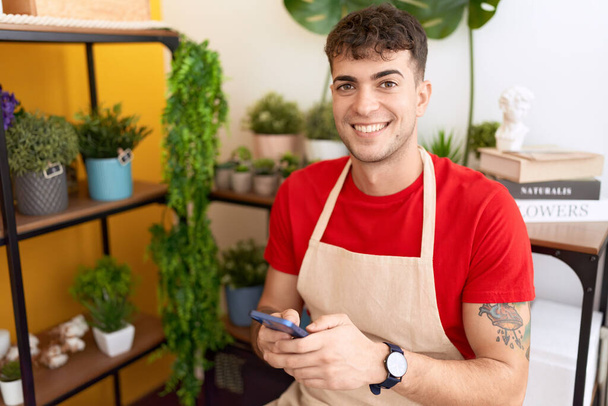 Young hispanic man florist smiling confident using smartphone at flower shop - Foto, afbeelding