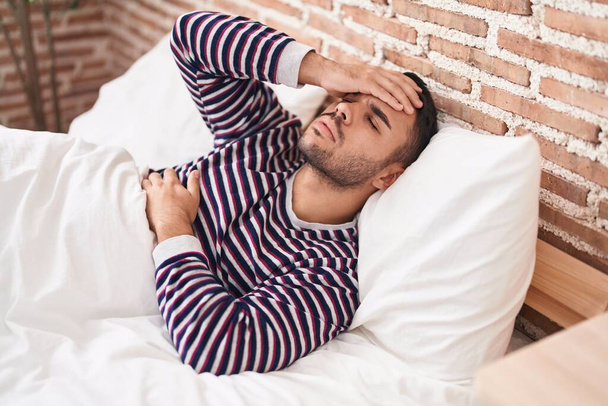 Young hispanic man stressed lying on bed at bedroom - Fotó, kép