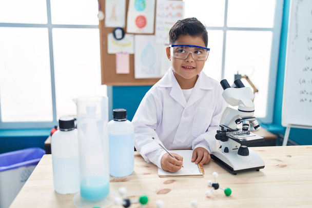 Entzückender hispanischer Junge mit Mikroskop-Notizen im Labor-Klassenzimmer - Foto, Bild