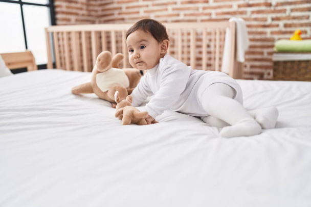 Adorable hispanic baby lying on bed with relaxed expression at bedroom - Photo, Image