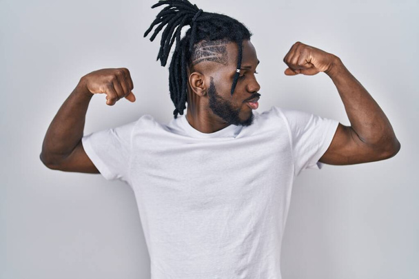 Uomo africano con dreadlocks indossare casual t shirt su sfondo bianco mostrando muscoli braccia sorridente orgoglioso. concetto di fitness.  - Foto, immagini