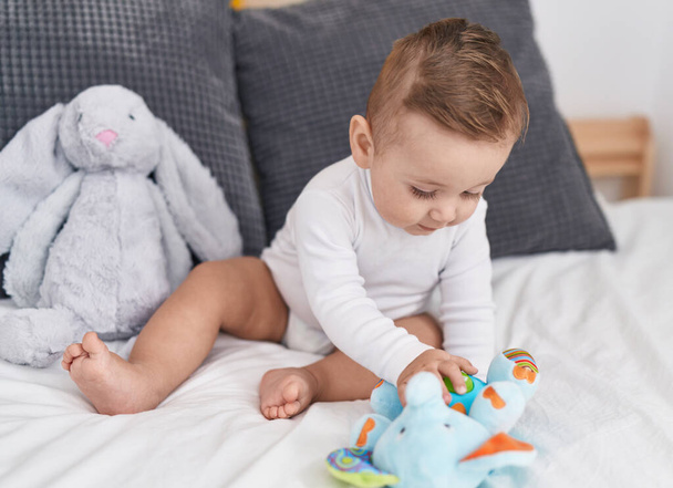 Adorable caucasian baby playing with elephant toy sitting on bed at home - Photo, Image
