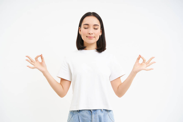 Peaceful smiling asian woman, standing calm and relaxed, holds hands in zen, meditation pose, isolated over white background. - Φωτογραφία, εικόνα