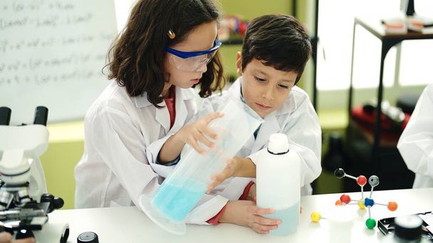 Liebenswerte Jungen und Mädchen Schülerin gießt Flüssigkeit auf Reagenzglas im Labor Klassenzimmer - Foto, Bild