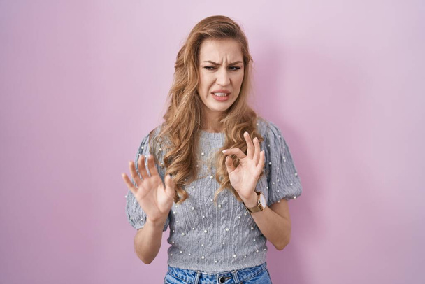 Beautiful blonde woman standing over pink background disgusted expression, displeased and fearful doing disgust face because aversion reaction.  - Foto, Imagem