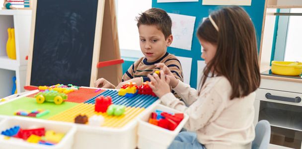 Uroczy chłopiec i dziewczyna bawią się klockami budowlanymi siedzącymi na stole w przedszkolu - Zdjęcie, obraz