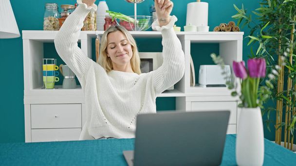 Young blonde woman using laptop dancing at dinning room - Fotó, kép
