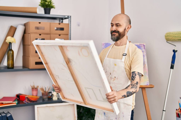 Молодий лисий чоловік художник посміхається впевнено дивиться малюнок на художній студії
 - Фото, зображення